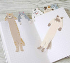 All six ALTA Hugging Cat bookmark designs hanging out of an open notebook